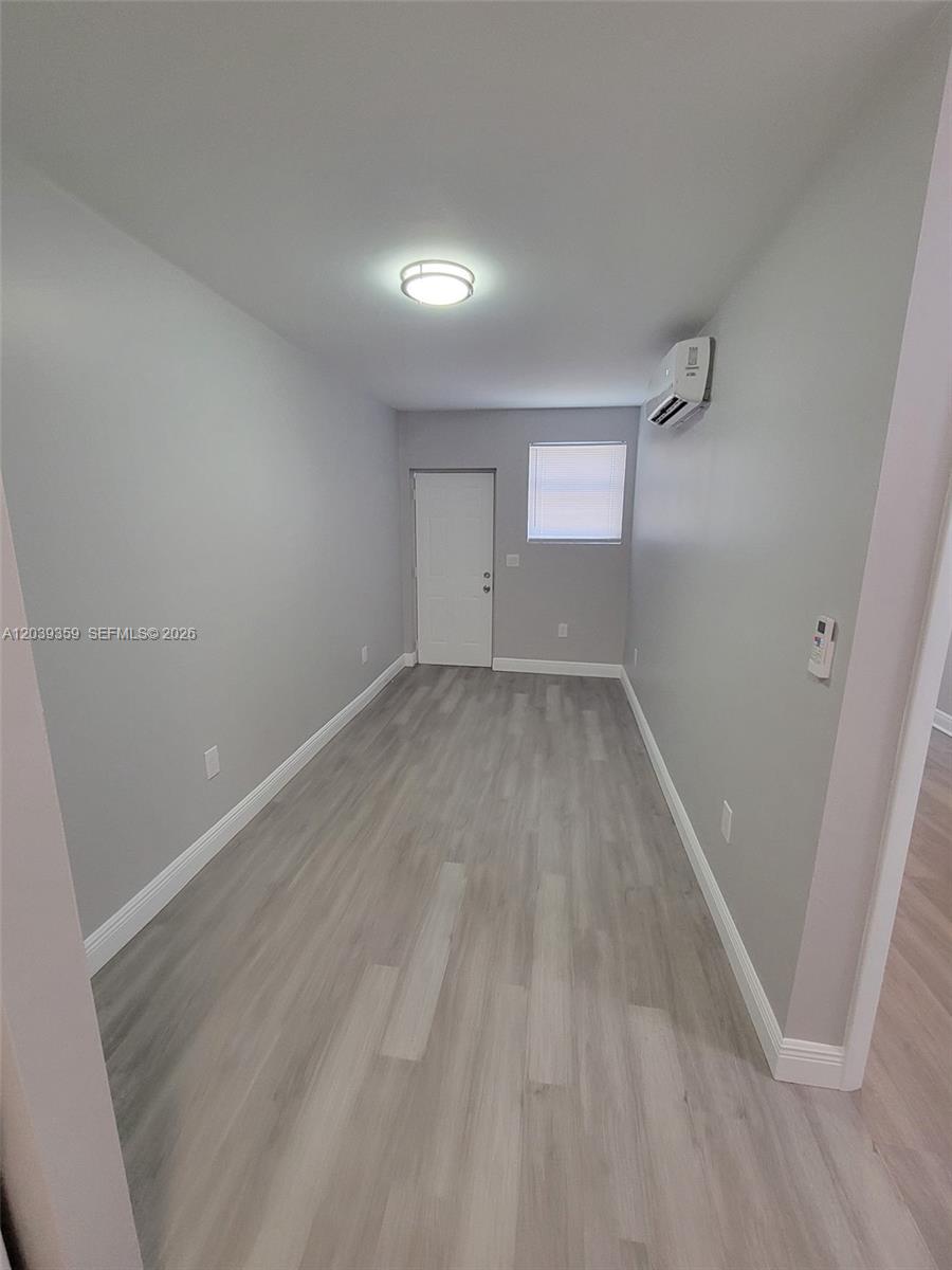 A small, empty room features light gray walls, wood-look flooring, a window, and a wall-mounted AC — 1740 NW 1st Pl # 5, Miami FL 33136, MIAMI, FL
