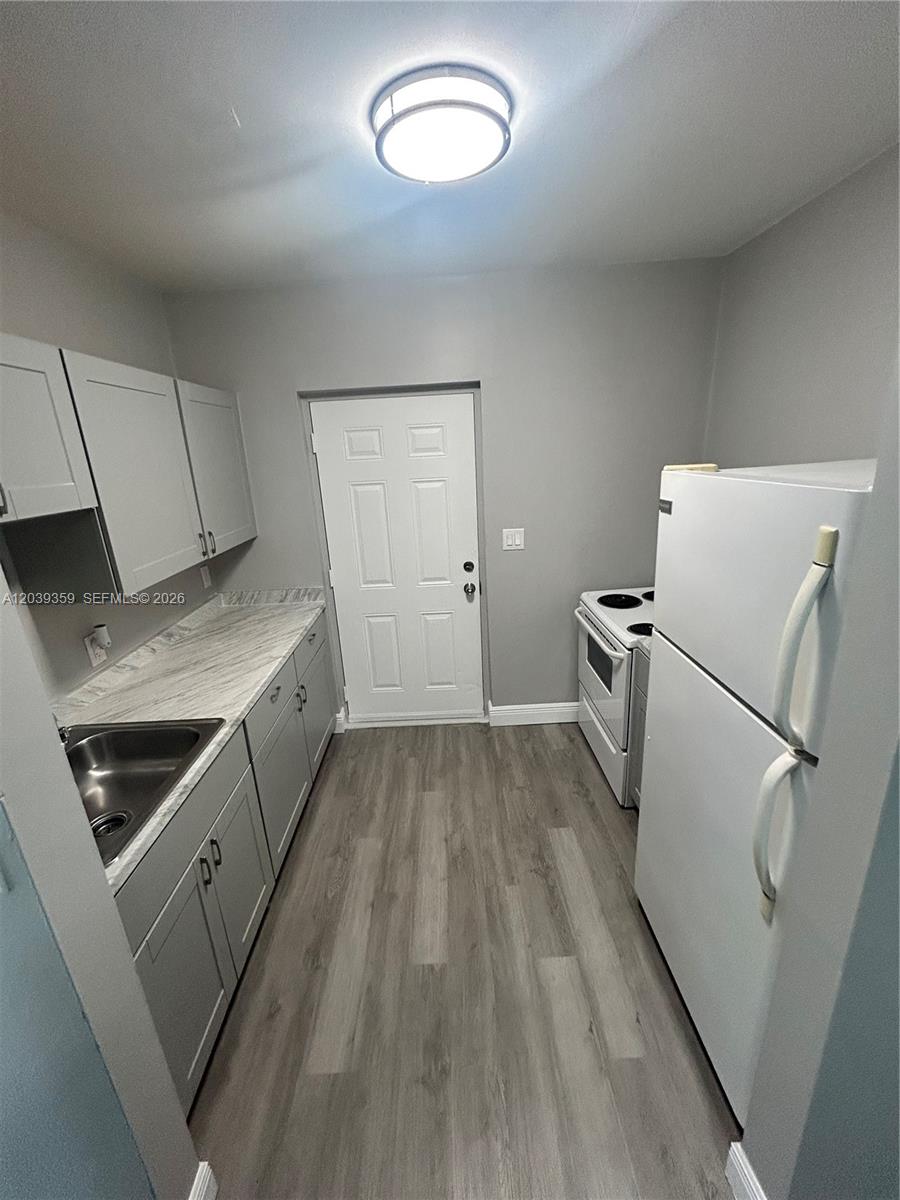 A galley kitchen features gray cabinets, white appliances, wood-look flooring, and a white exterior door — 1740 NW 1st Pl # 5, Miami FL 33136, MIAMI, FL