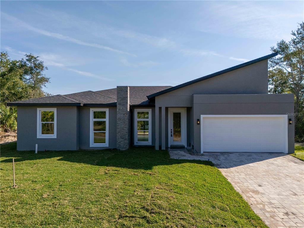 A modern single-story house with a gray exterior, stone chimney, and a two-car garage — 70 MCDILL DRIVE, PORT CHARLOTTE, FL