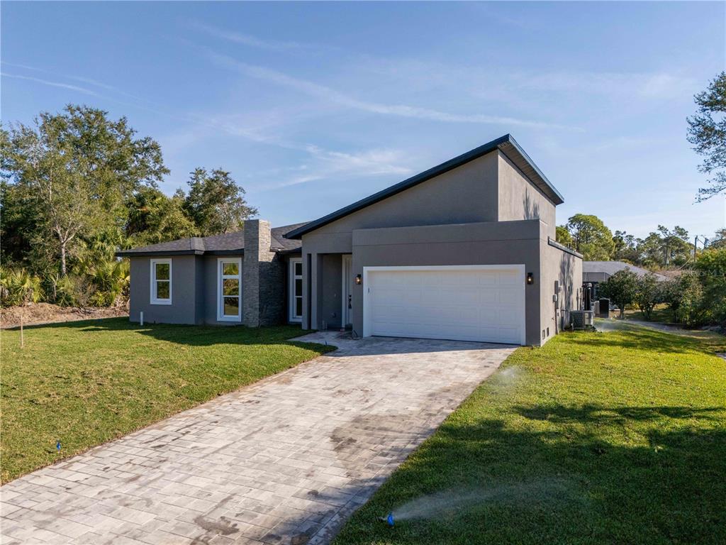 A modern gray house with a paved driveway and a two-car garage under a clear sky — 70 MCDILL DRIVE, PORT CHARLOTTE, FL