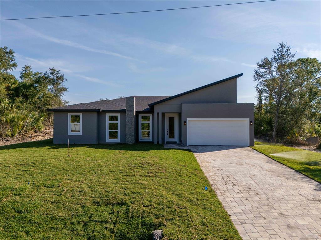 A modern, single-story house with a gray exterior, a white garage door, and a paved driveway — 70 MCDILL DRIVE, PORT CHARLOTTE, FL