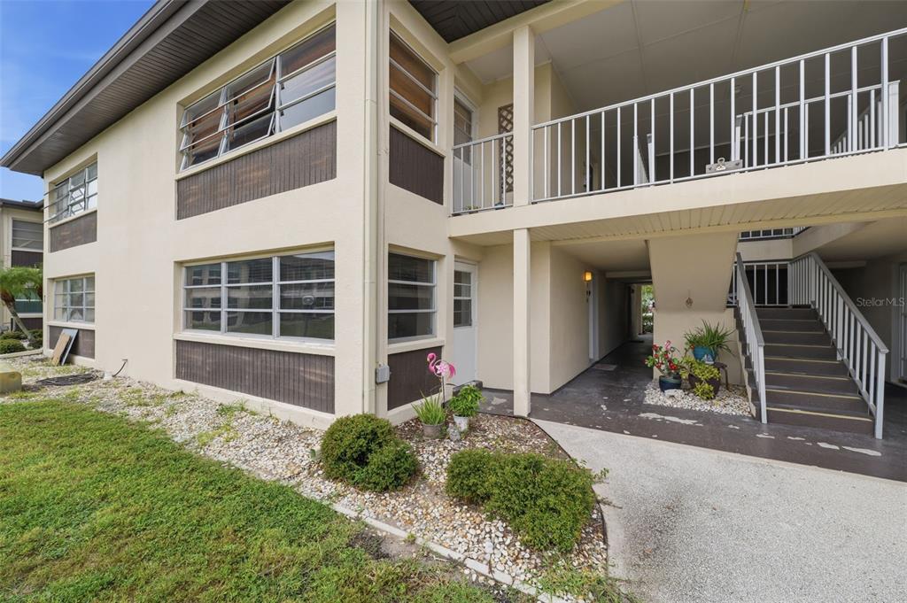 A two-story apartment building exterior features beige stucco walls, brown accents, and an outdoor staircase — 5242 OPAL LANE UNIT 104, NEW PORT RICHEY, FL