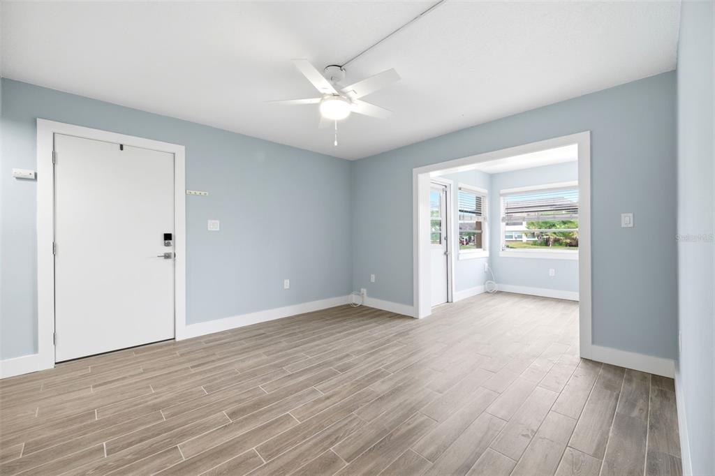 A light blue room with wood-look tile flooring, a ceiling fan, and an adjacent sunroom — 5242 OPAL LANE UNIT 104, NEW PORT RICHEY, FL