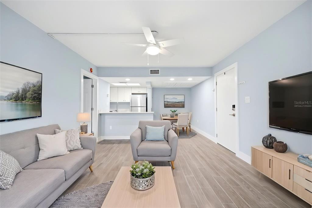 A living room with light blue walls, gray tile flooring, and a kitchen in the background — 5242 OPAL LANE UNIT 104, NEW PORT RICHEY, FL