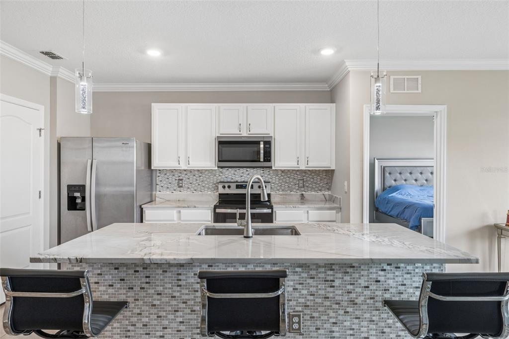 A kitchen features a marble-topped island, white cabinets, stainless steel appliances, and a mosaic backsplash — 109 SOFIA LANE, LAKE ALFRED, FL
