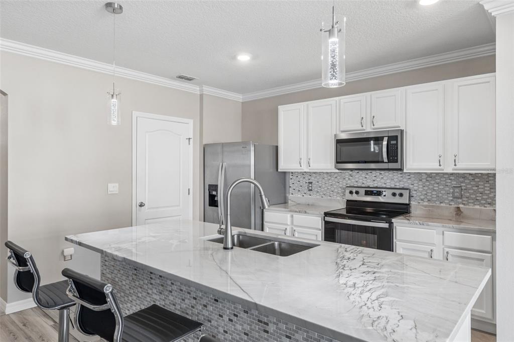 A modern kitchen features white cabinets, stainless steel appliances, and a marble-topped island with seating — 109 SOFIA LANE, LAKE ALFRED, FL