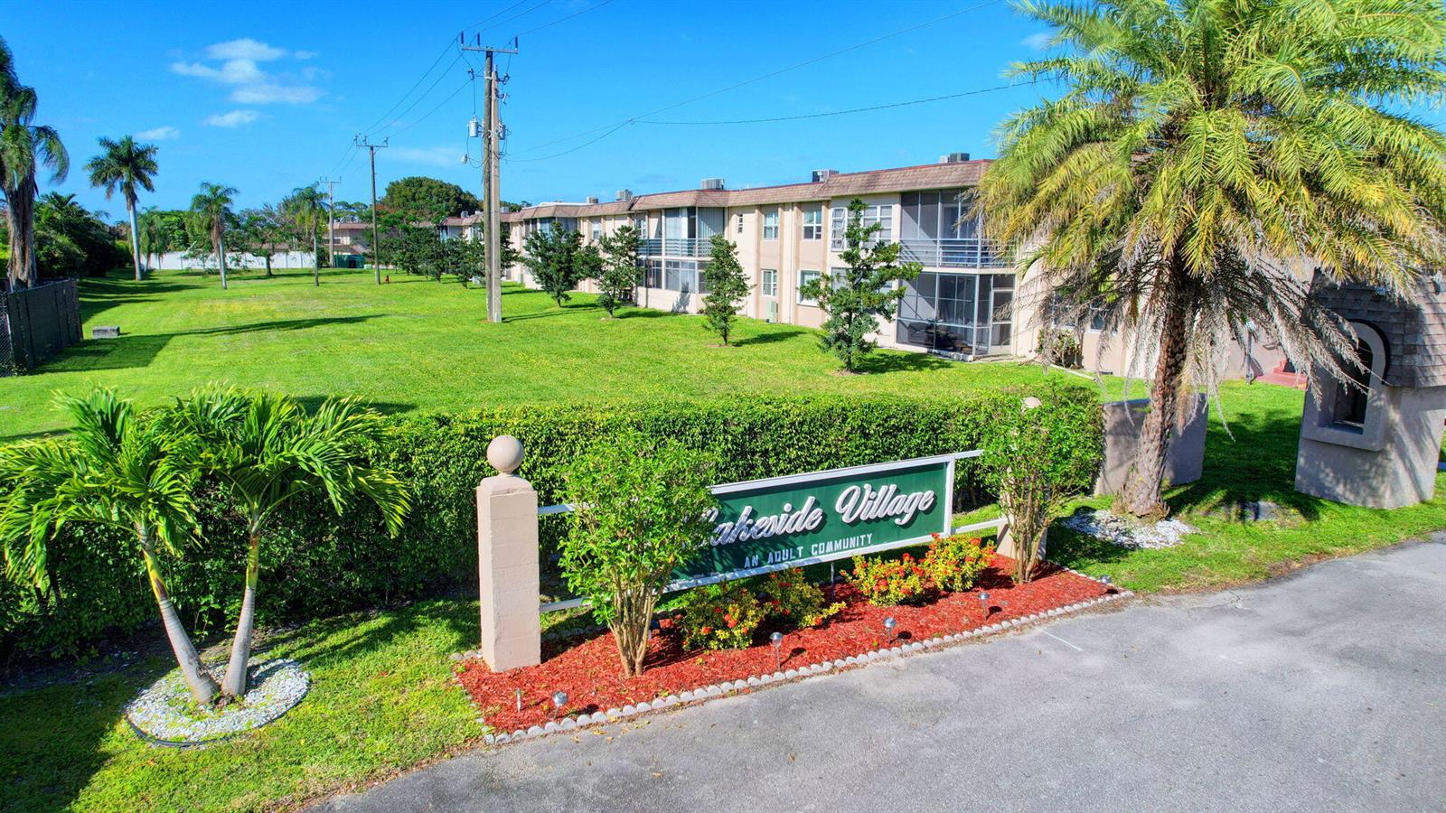 An exterior view of the Lakeside Village adult community sign and adjacent apartment building — 725 Lori Drive # 106, Palm Springs FL 33461, PALM SPRINGS, FL
