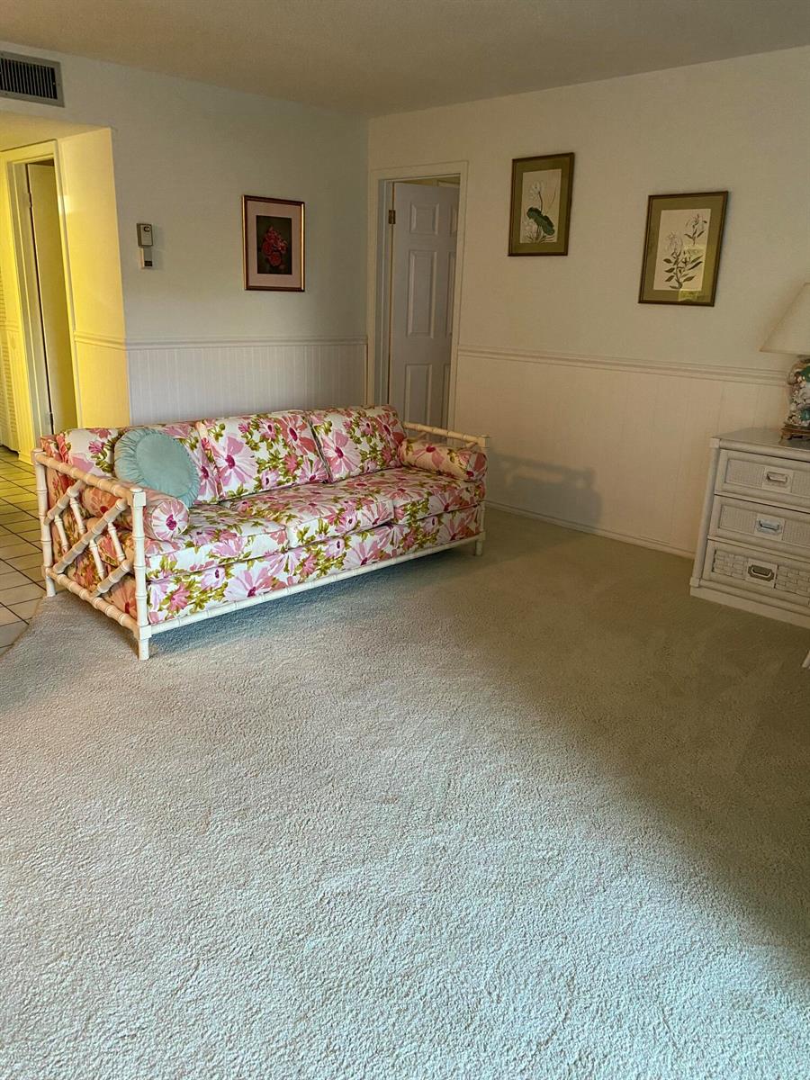 A living room features a floral sofa, beige carpeting, white wainscoting, and framed wall art — 725 Lori Drive # 106, Palm Springs FL 33461, PALM SPRINGS, FL