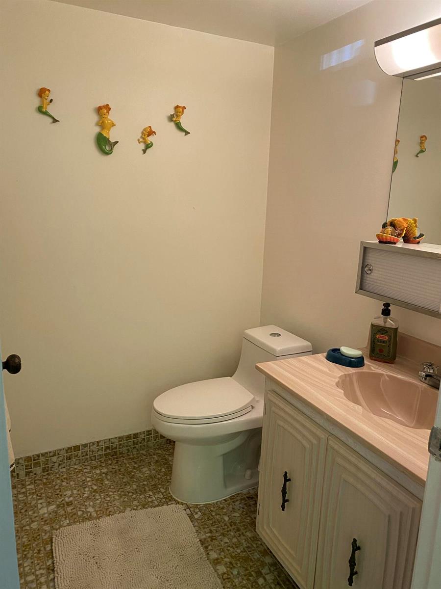 A bathroom features a pink vanity, a white toilet, and mermaid wall decor — 725 Lori Drive # 106, Palm Springs FL 33461, PALM SPRINGS, FL