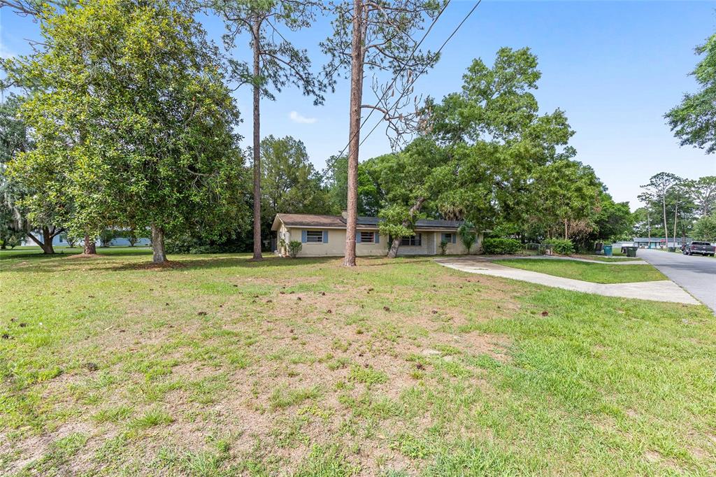 A single-story house with a beige exterior sits on a large, grassy lot with trees — 1921 NE 49TH AVENUE, OCALA, FL
