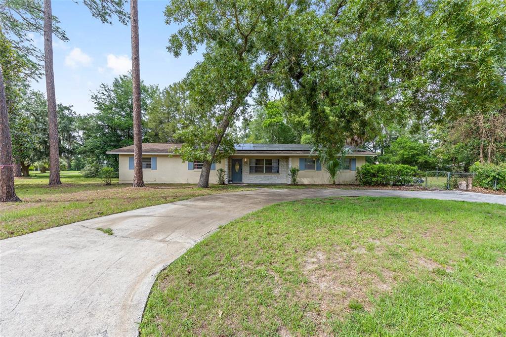 A single-story house with a concrete driveway, solar panels, and large trees in the yard — 1921 NE 49TH AVENUE, OCALA, FL