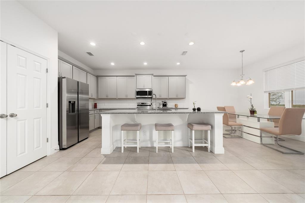 A modern kitchen features light gray cabinetry, stainless steel appliances, a granite island, and tile flooring — 1867 LAKE INDIGO ROAD, GROVELAND, FL