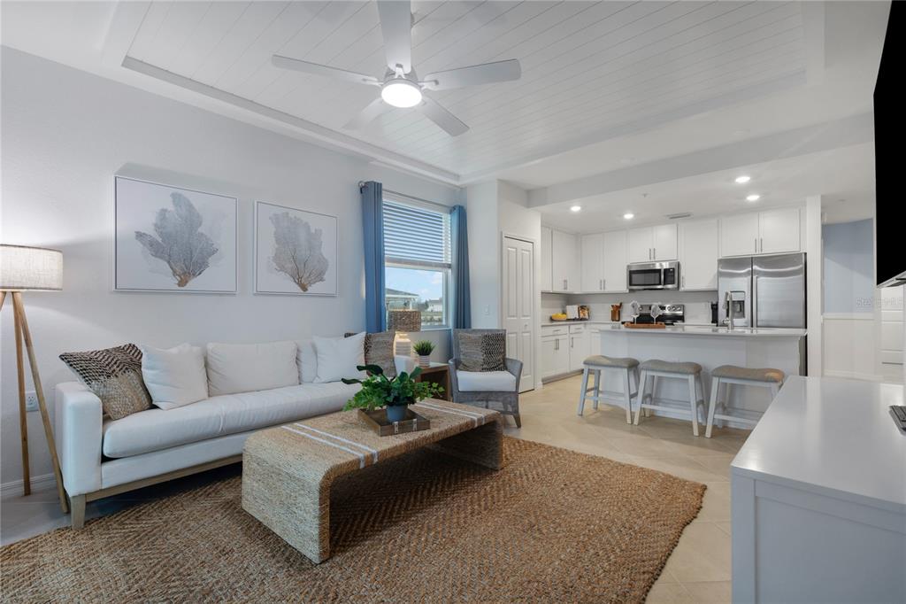 A bright open-concept living room and kitchen featuring white cabinetry, a ceiling fan, and furniture — 17630 OPAL SAND DRIVE UNIT 108, VENICE, FL