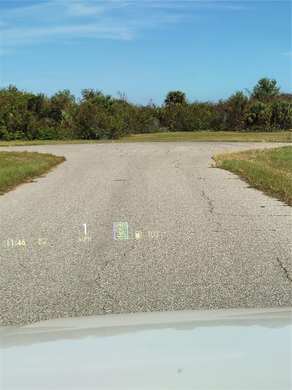 A view from a vehicle windshield showing a paved road leading toward a grassy area — 9 HYDE COURT, ROTONDA WEST, FL