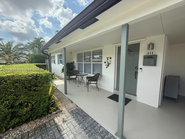 A covered front porch features a gray door, two chairs, and a small table — 330 NE 48th St, Oakland Park FL 33334, OAKLAND PARK, FL