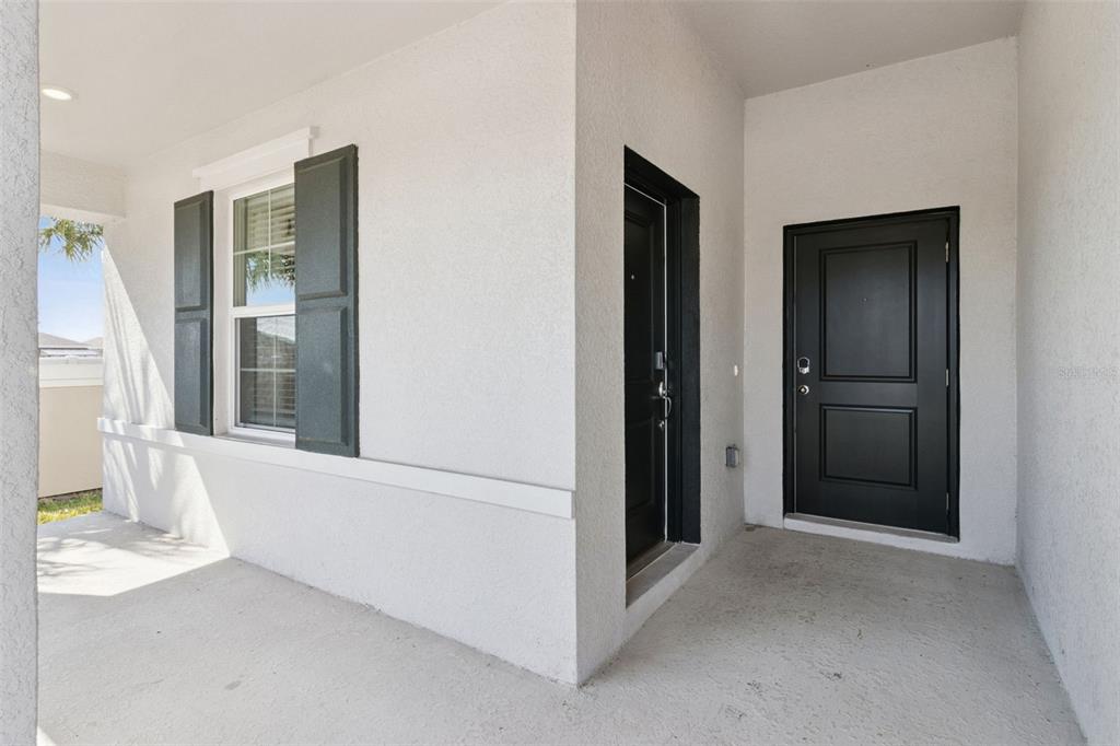 A covered porch features white stucco walls, a window with dark shutters, and two black doors — 101 KAYAK AVENUE, HAINES CITY, FL