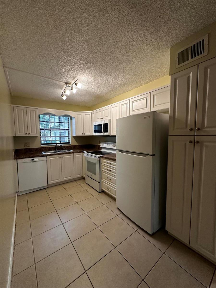 A kitchen features white cabinets, white appliances, tile flooring, and a window above the sink — 321 Olivewood Place # 121, Boca Raton FL 33431, BOCA RATON, FL