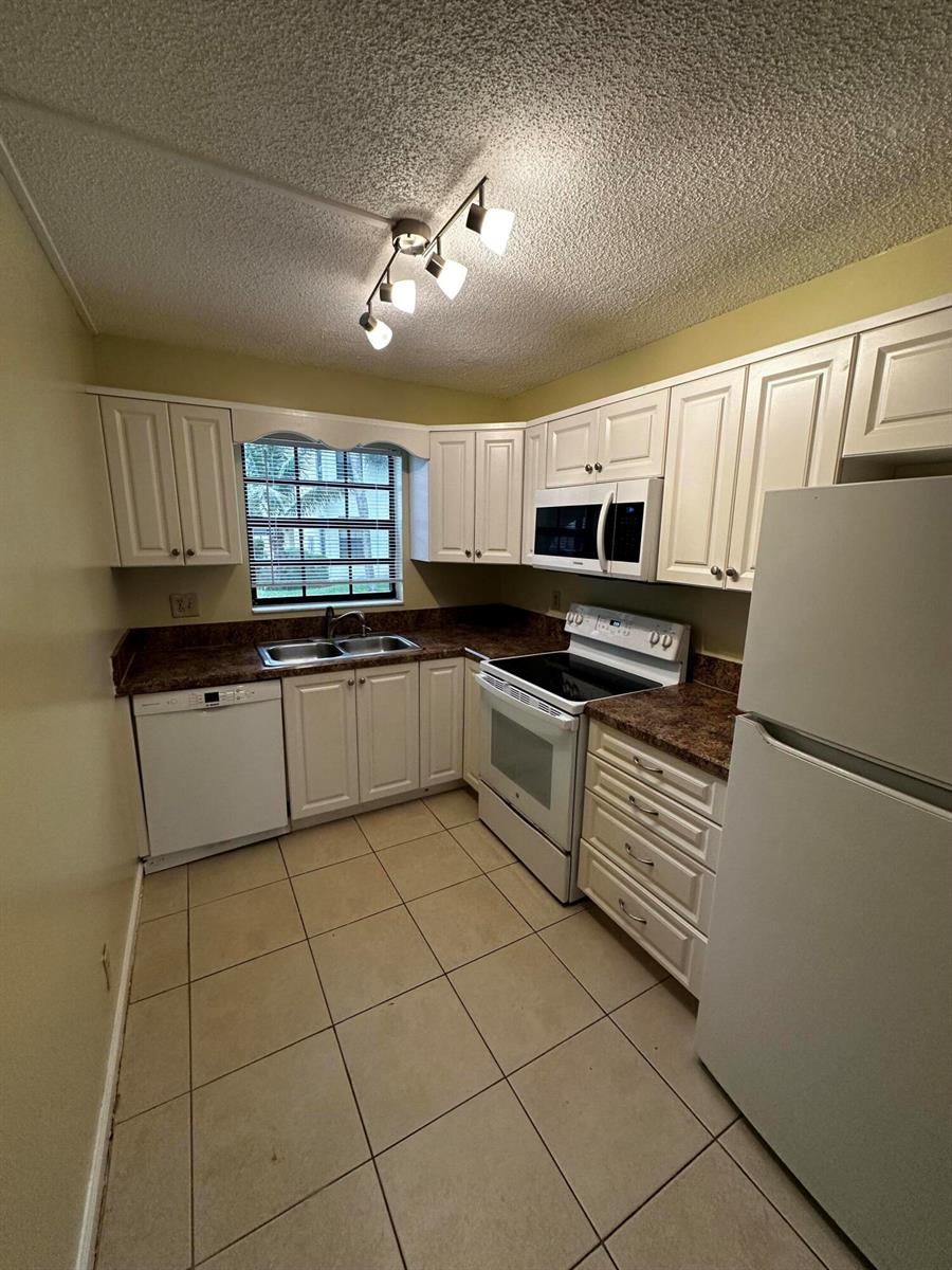 A view of an open-concept living area with tile flooring leading into a white kitchen — 321 Olivewood Place # 121, Boca Raton FL 33431, BOCA RATON, FL