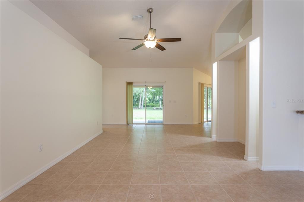 An empty living area with beige tile floors, a ceiling fan, and sliding glass doors — 3 ZODIAC PLACE, PALM COAST, FL
