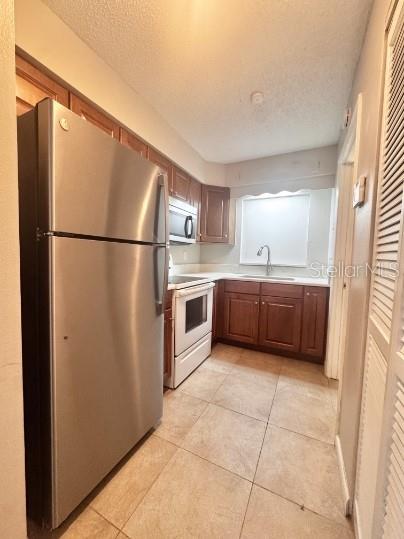 A kitchen features stainless steel appliances, wood cabinets, and light-colored tile flooring — 1340 ANDERSON STREET UNIT 1350, CLERMONT, FL