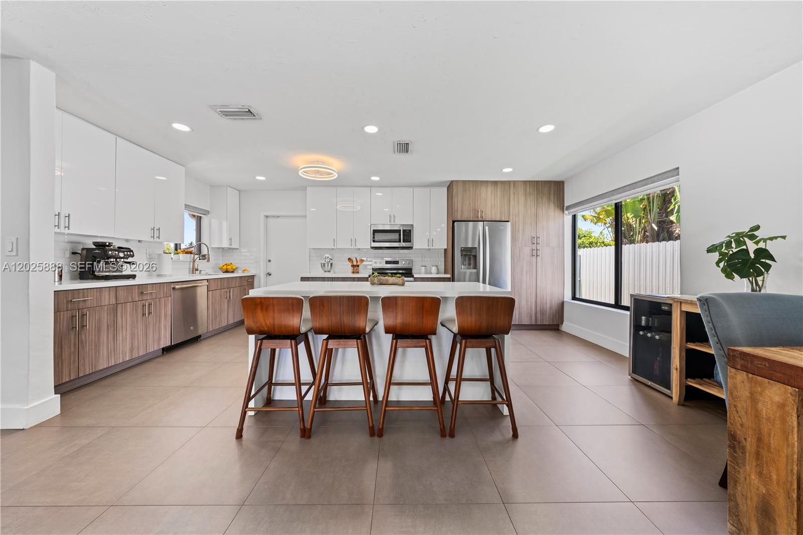 A modern kitchen features white and wood-toned cabinetry, a central island with four stools, and tile flooring — 12731 SW 47th Ter, Miami FL 33175, MIAMI, FL