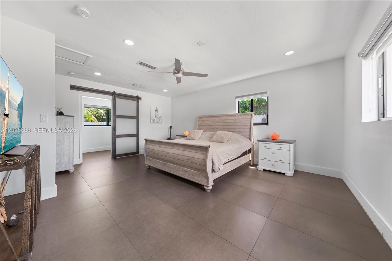 This bedroom features a light wood bed frame, tile flooring, and a sliding barn door — 12731 SW 47th Ter, Miami FL 33175, MIAMI, FL