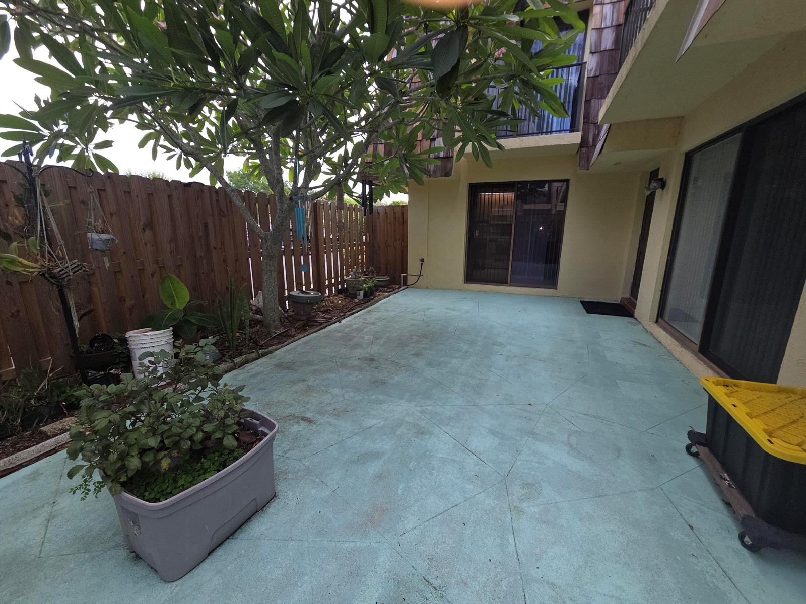 A paved patio area features a large tree, a wooden fence, and sliding glass doors — 1170 6th Avenue # 3a, Vero Beach FL 32960, VERO BEACH, FL