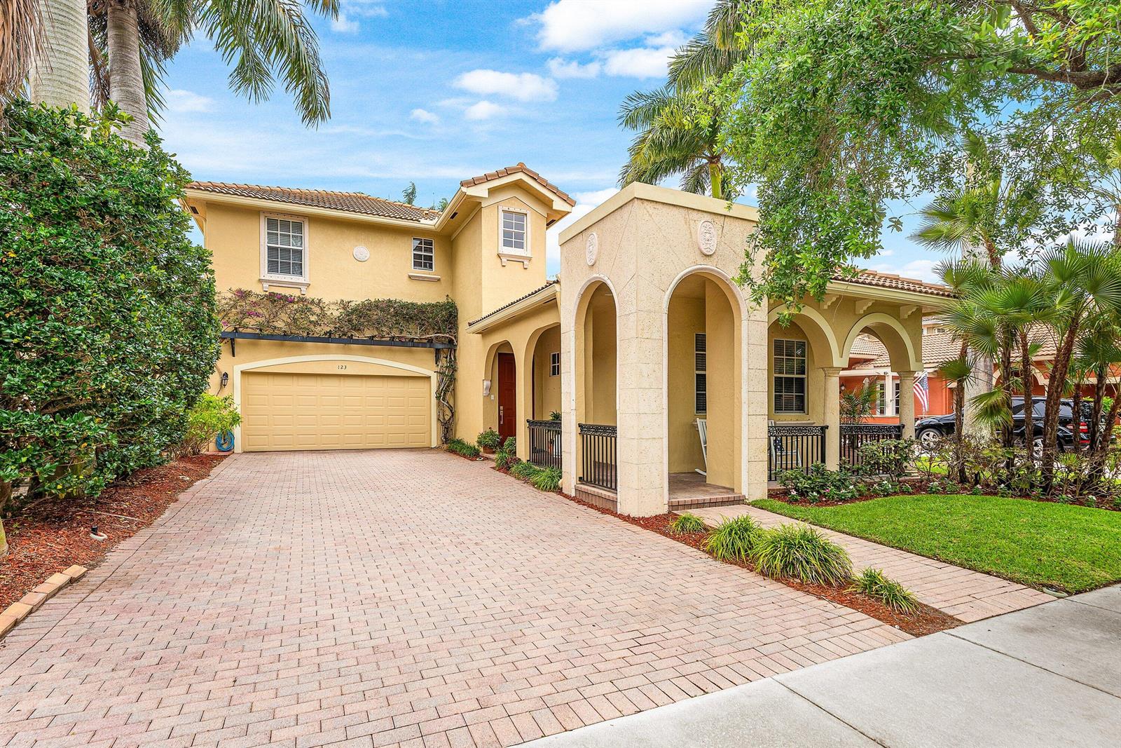 A two-story yellow house with a paved driveway, arched entryway, and a two-car garage — 123 Via Castilla, Jupiter FL 33458, JUPITER, FL