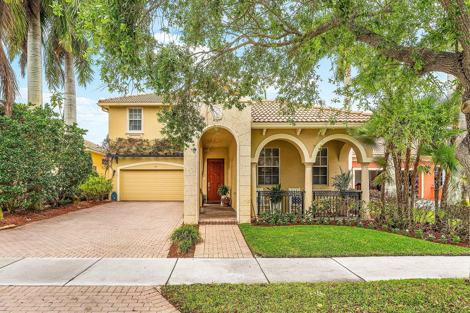 A two-story yellow stucco house features a tiled roof, arched entryway, and a paved driveway — 123 Via Castilla, Jupiter FL 33458, JUPITER, FL