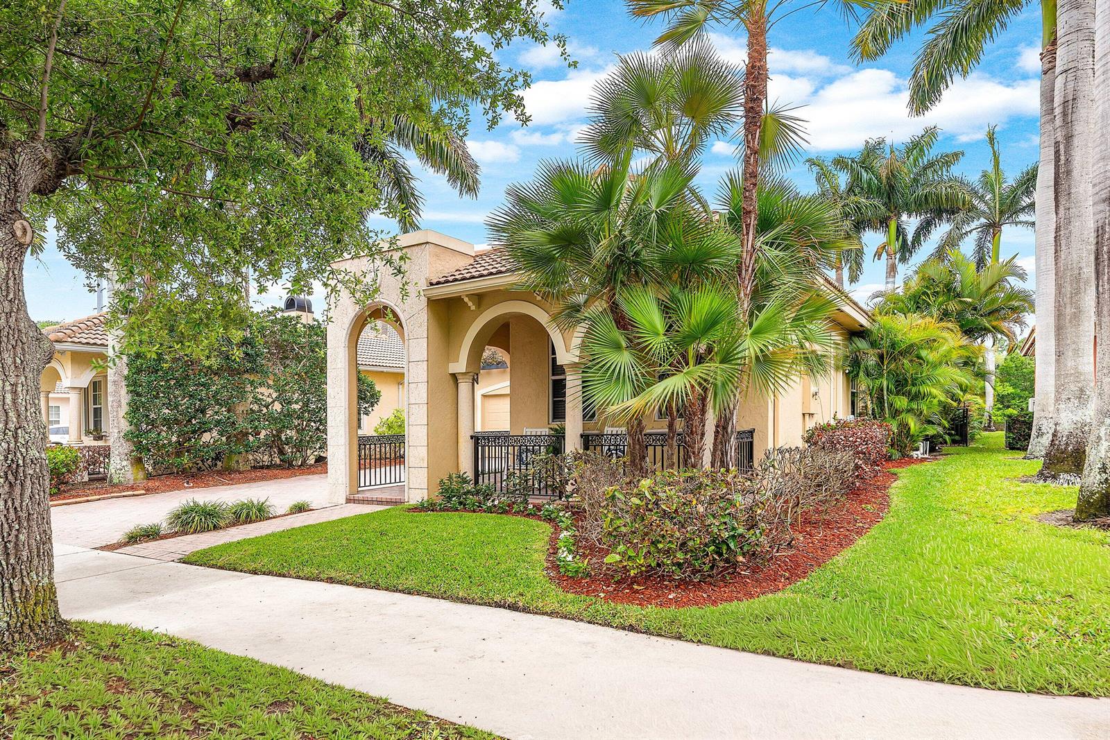 A tan stucco house features an arched entryway, a covered porch, and lush tropical landscaping — 123 Via Castilla, Jupiter FL 33458, JUPITER, FL