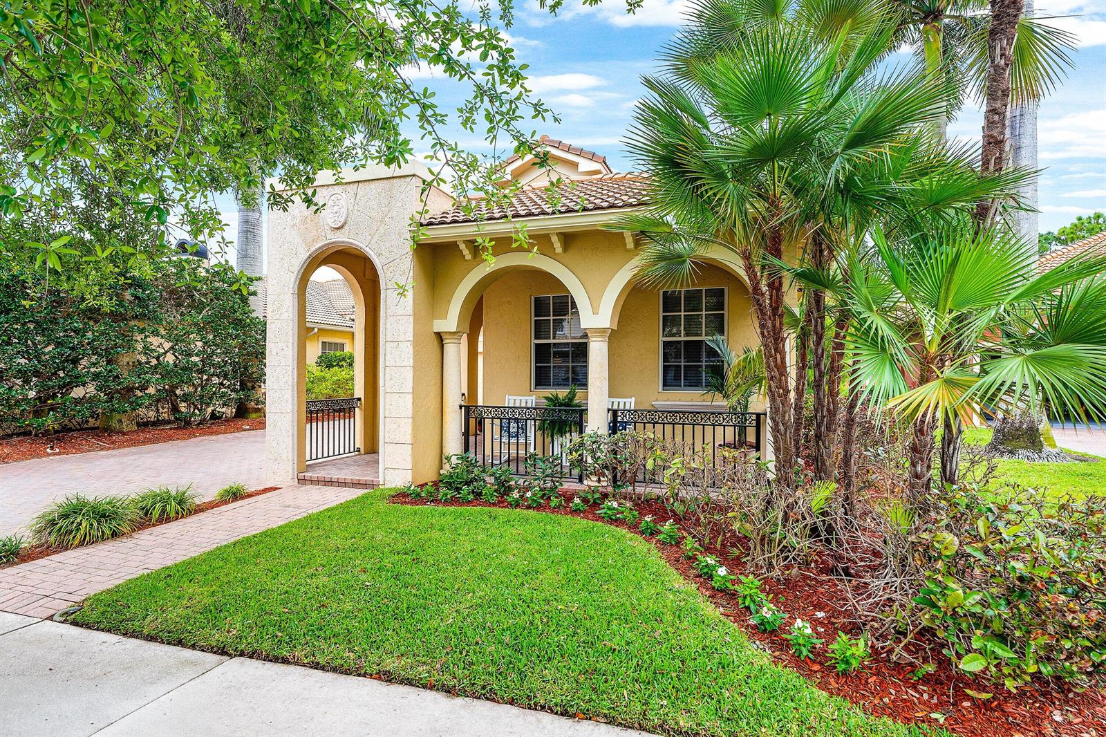 A tan stucco house features a covered front porch with arched openings and black railings — 123 Via Castilla, Jupiter FL 33458, JUPITER, FL