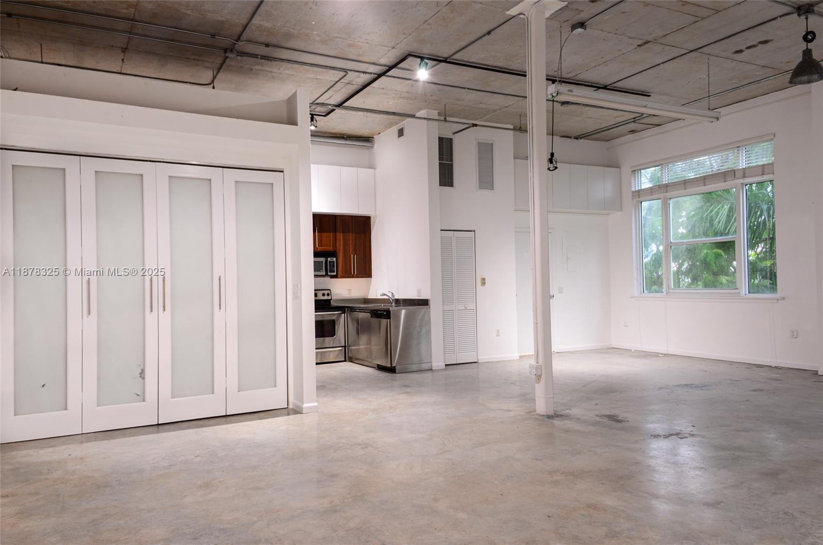 An open-concept loft features a kitchen, concrete floors, exposed ceiling pipes, and large windows — 250 NW 23rd st # 308, Miami FL 33127, MIAMI, FL