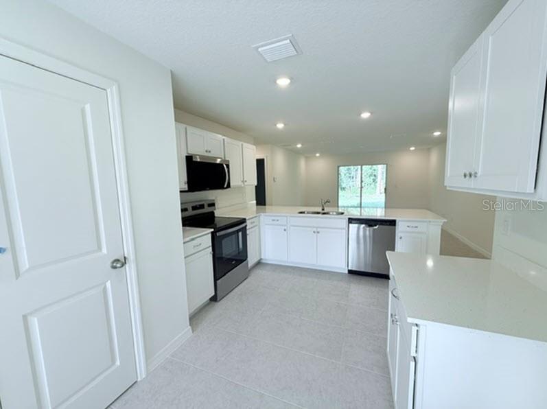 A kitchen features white cabinets, stainless steel appliances, and light-colored countertops — 32 KALAMAZOO TRAIL, PALM COAST, FL