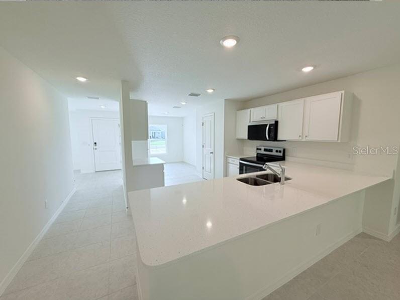 A kitchen with white cabinets, quartz countertops, and stainless steel appliances opens to a hallway — 32 KALAMAZOO TRAIL, PALM COAST, FL