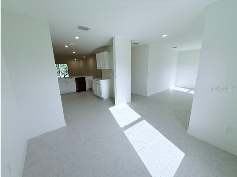 An open-concept room with white walls, light tile flooring, and a kitchen in the background — 32 KALAMAZOO TRAIL, PALM COAST, FL