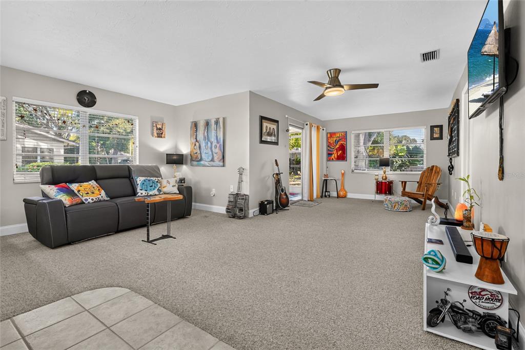 A living room with gray carpet, a dark sofa, musical decor, and a wall-mounted television — 4549 TIPPECANOE TRAIL UNIT 20, SARASOTA, FL