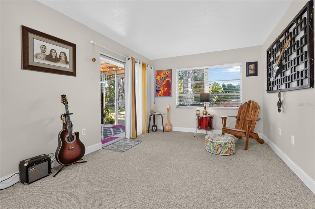A carpeted living room features a guitar, a wooden chair, and a sliding glass door — 4549 TIPPECANOE TRAIL UNIT 20, SARASOTA, FL