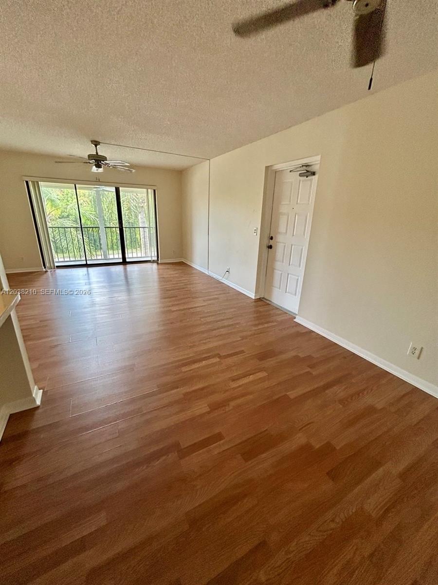 An empty living room features wood-look flooring, a ceiling fan, and a sliding glass door — 1113 Green Pine Blvd # H2, West Palm Beach FL 33409, WEST PALM BEACH, FL