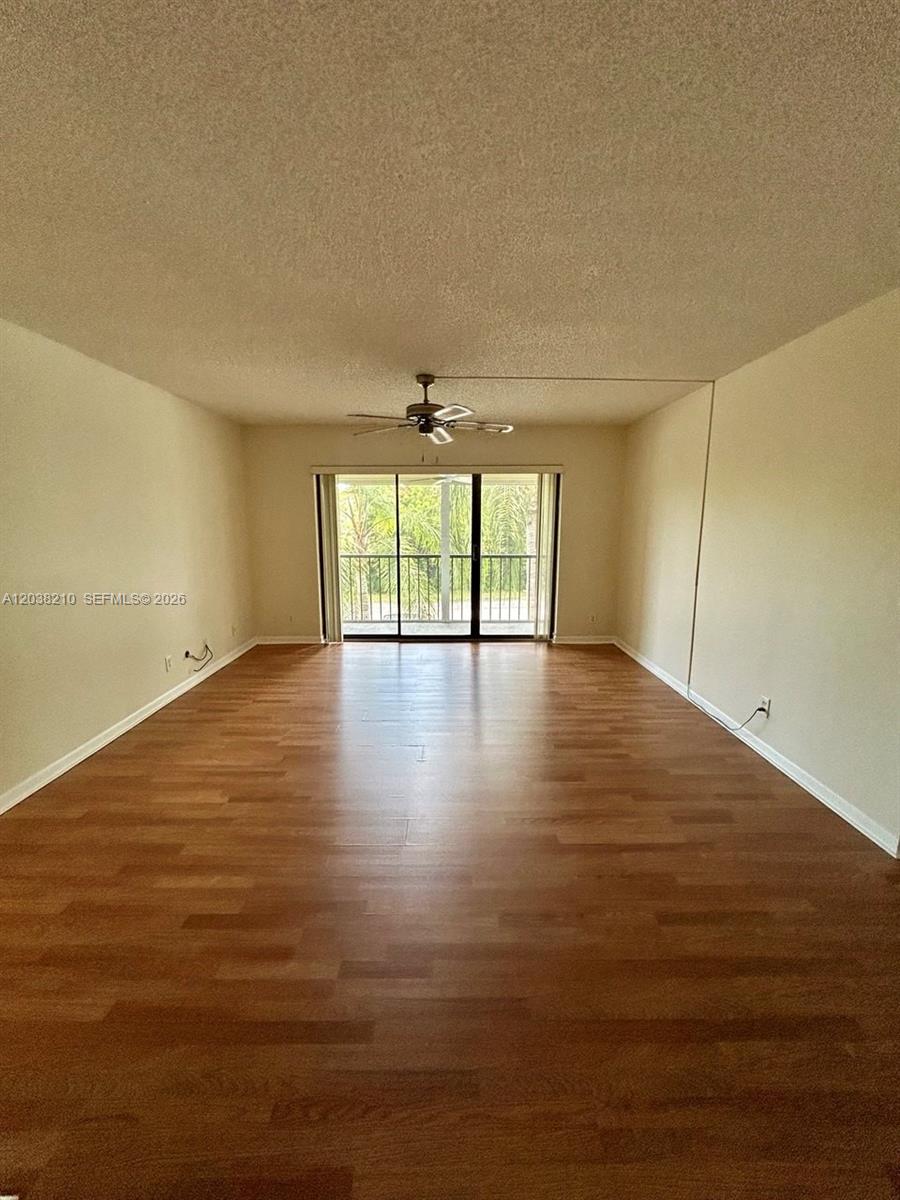 An empty living room features wood-look flooring, a ceiling fan, and sliding glass balcony doors — 1113 Green Pine Blvd # H2, West Palm Beach FL 33409, WEST PALM BEACH, FL