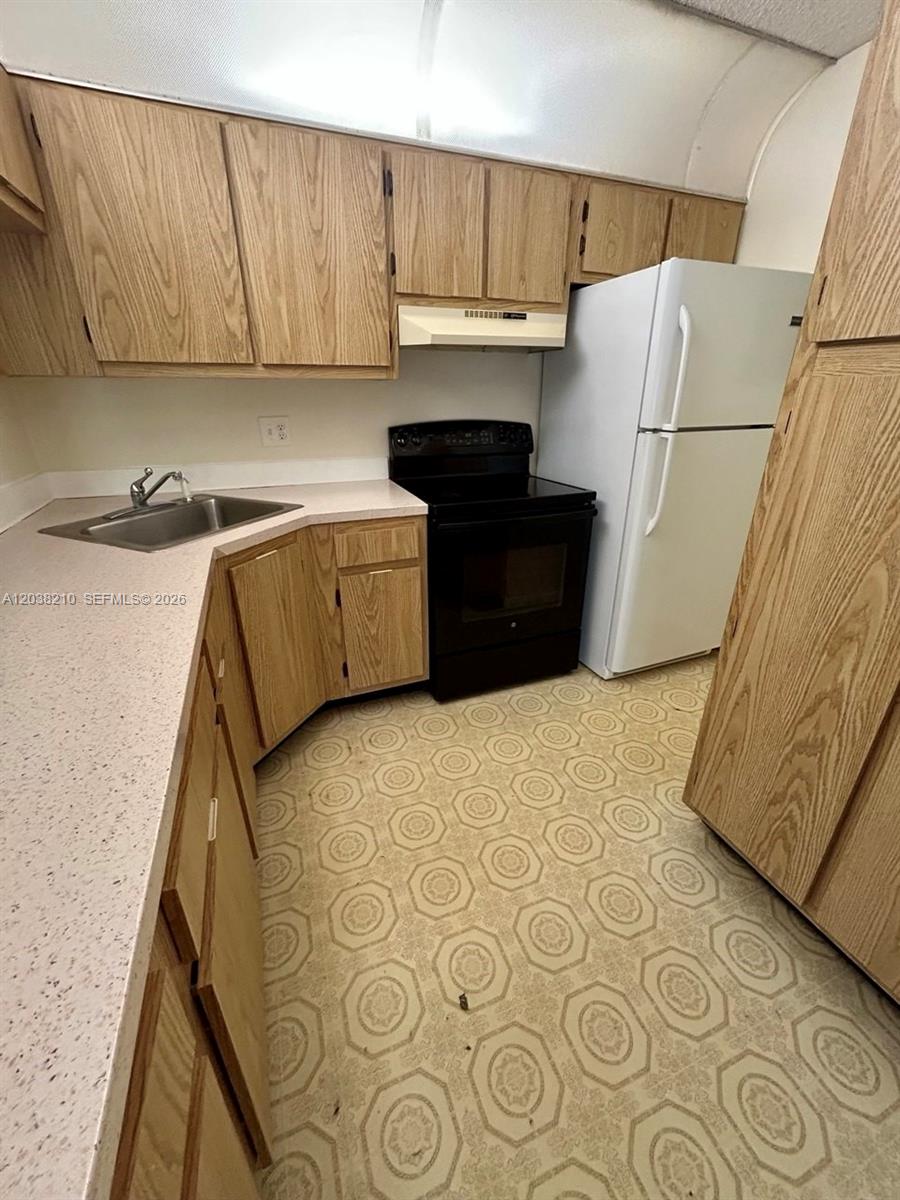 A kitchen features oak cabinets, a black stove, a white refrigerator, and patterned vinyl flooring — 1113 Green Pine Blvd # H2, West Palm Beach FL 33409, WEST PALM BEACH, FL