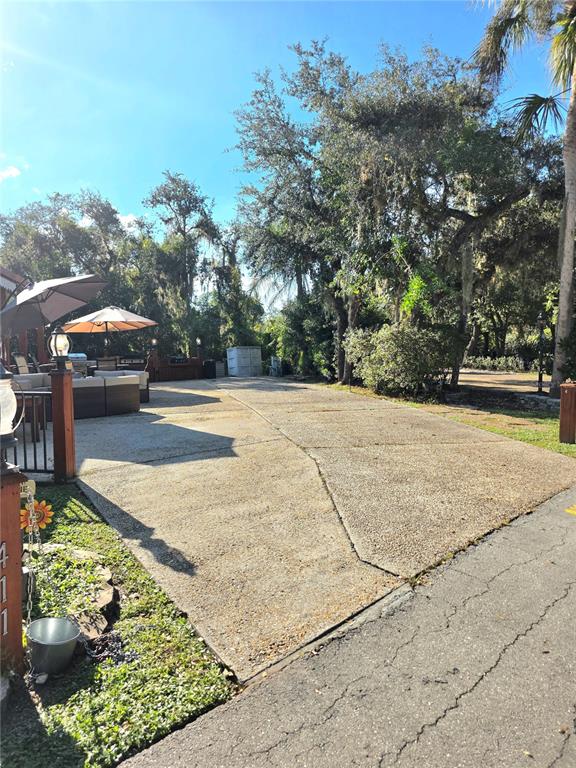 A concrete driveway leads toward an outdoor patio area with umbrellas and seating under trees — 411 LONGHORN DRIVE, LAKE WALES, FL