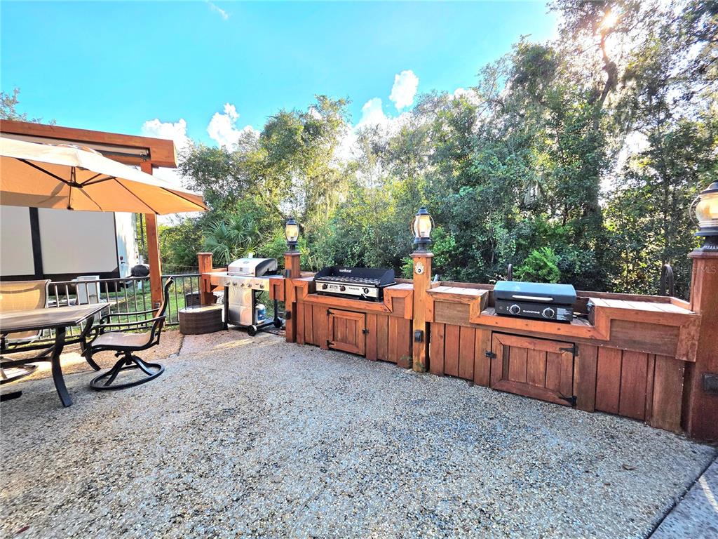 An outdoor patio features a wooden kitchen island with two grills and a dining area — 411 LONGHORN DRIVE, LAKE WALES, FL