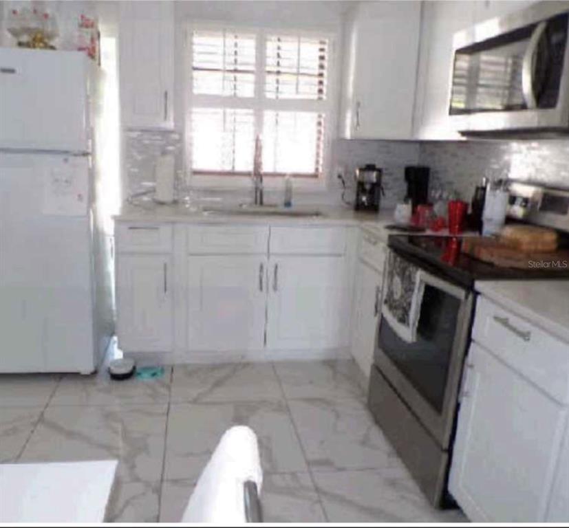 A kitchen features white cabinets, stainless steel appliances, and light-colored tile flooring — 3107 W OSBORNE AVENUE, TAMPA, FL