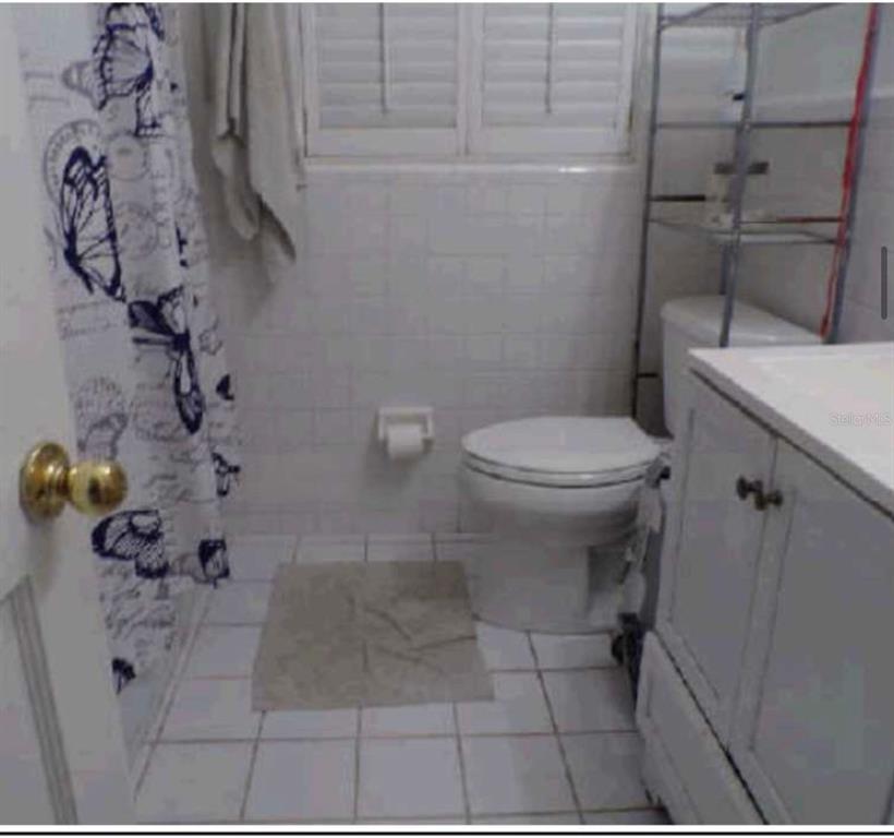 A small bathroom features white tiled walls, a white vanity, a toilet, and a shower curtain — 3107 W OSBORNE AVENUE, TAMPA, FL