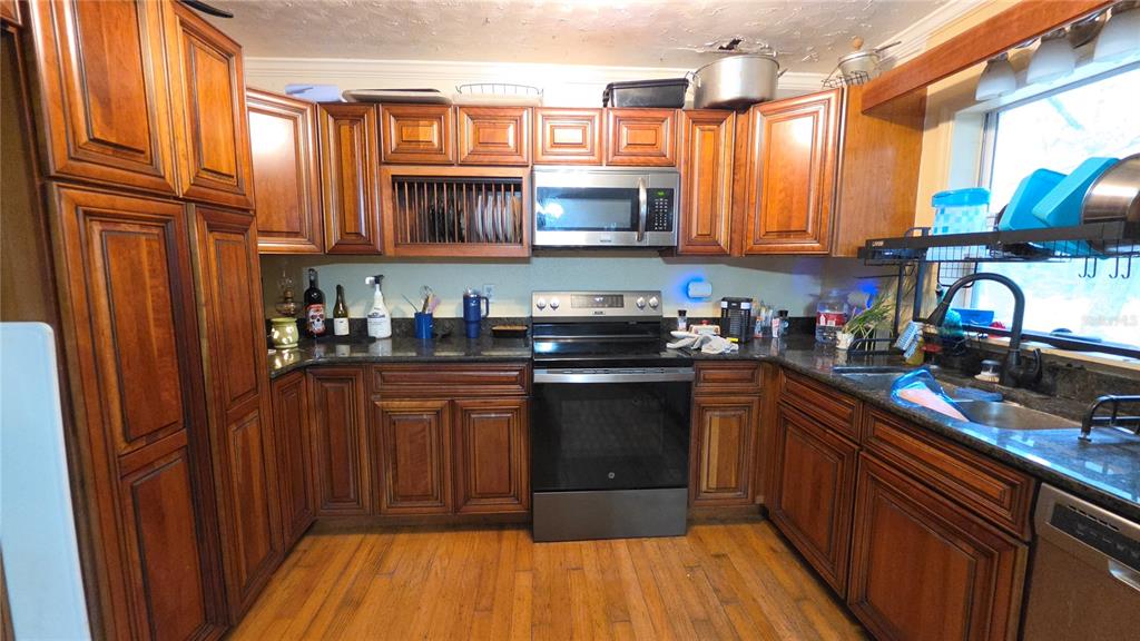 A kitchen features wood cabinets, dark countertops, stainless steel appliances, and hardwood flooring — 12590 NW 82ND COURT, CHIEFLAND, FL