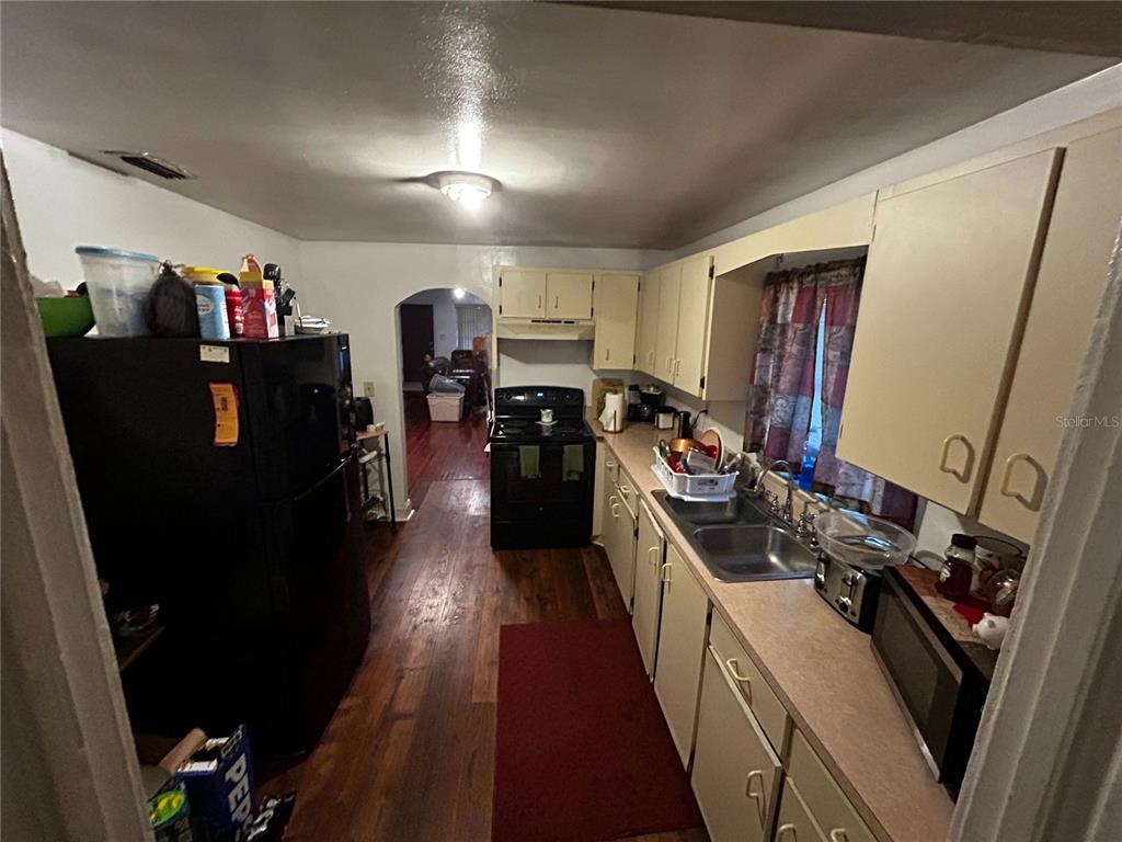 A kitchen features light-colored cabinets, a black refrigerator, a black stove, and wood flooring — 415 MODEL STREET, DAYTONA BEACH, FL