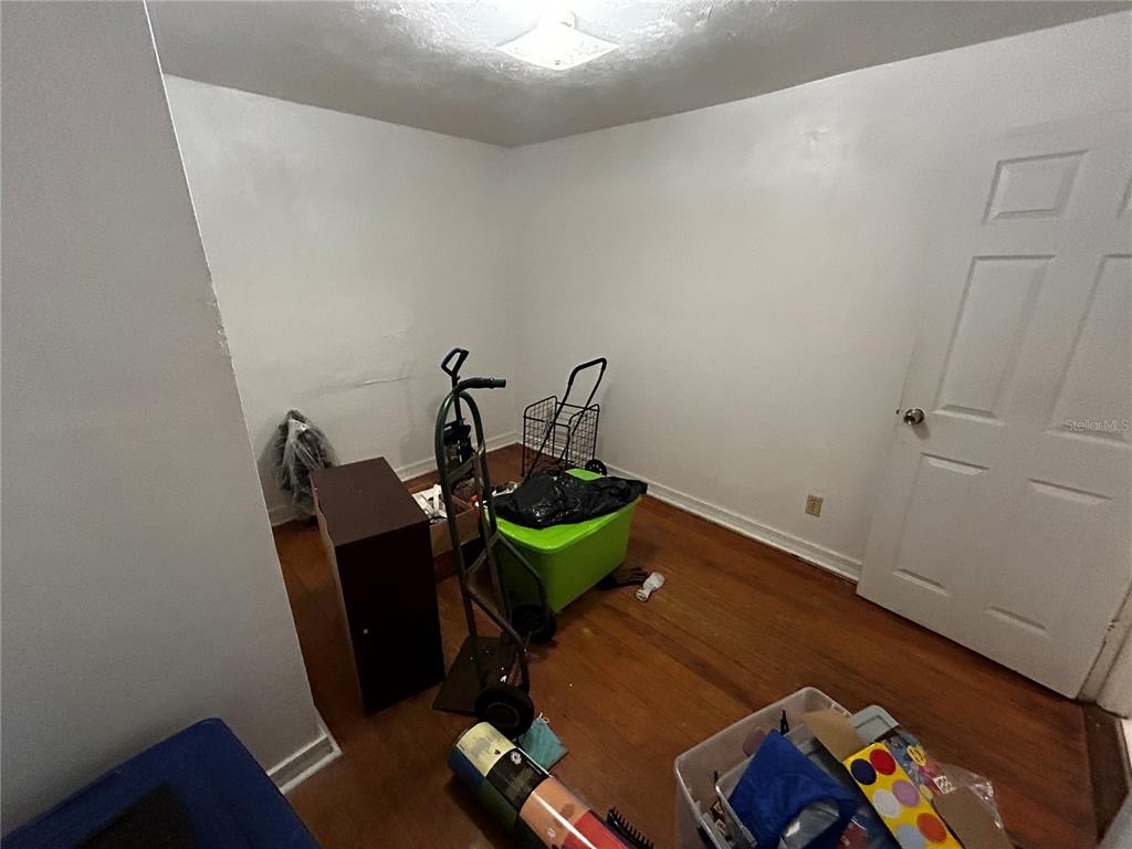 A small, sparsely furnished room with white walls, hardwood floors, and a closed white door — 415 MODEL STREET, DAYTONA BEACH, FL