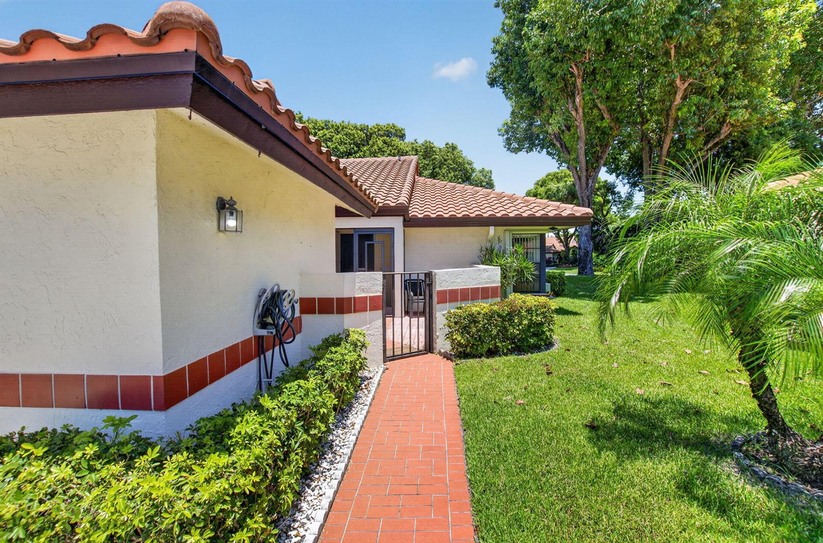 A red brick walkway leads to a gated entrance of a house with stucco walls — 10546 Beach Palm Court # B, Boynton Beach FL 33437, BOYNTON BEACH, FL