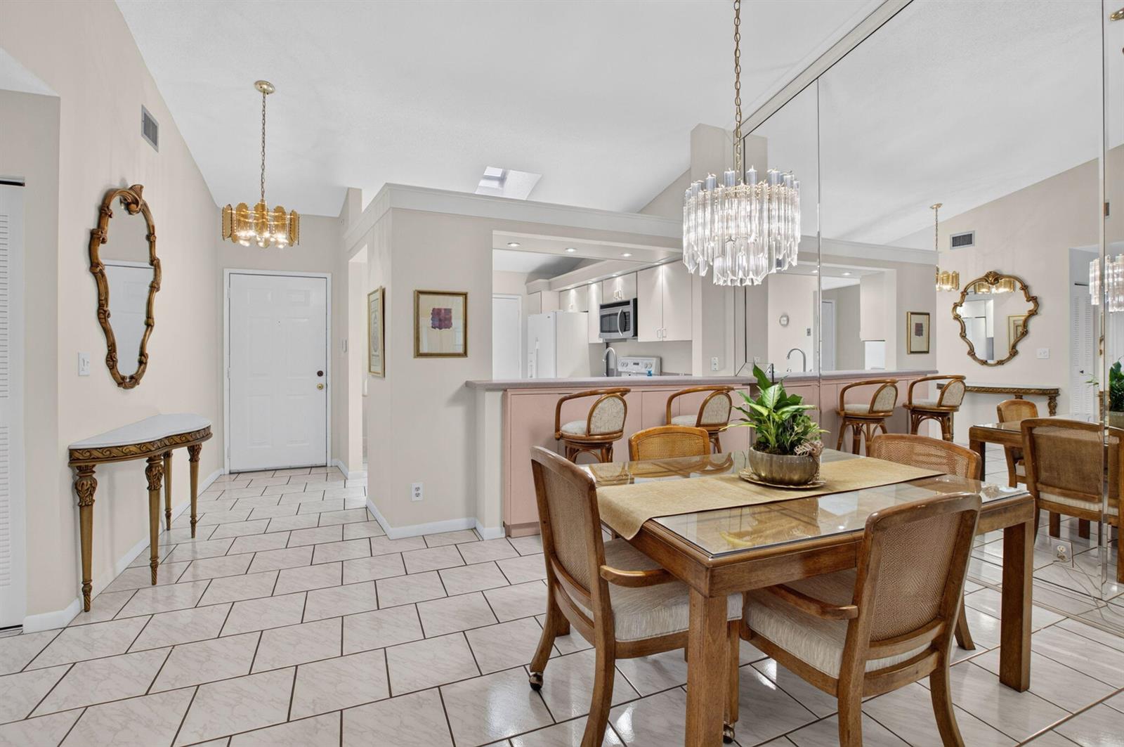 A dining area with a glass-top table, chandelier, and mirrored wall adjacent to a kitchen — 10546 Beach Palm Court # B, Boynton Beach FL 33437, BOYNTON BEACH, FL