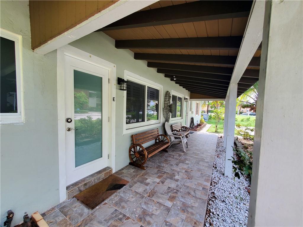 A covered patio with tiled flooring, a wooden wagon-wheel bench, and a glass-paneled entry door — 3204 NE 6th Street, Pompano Beach FL 33062, POMPANO BEACH, FL